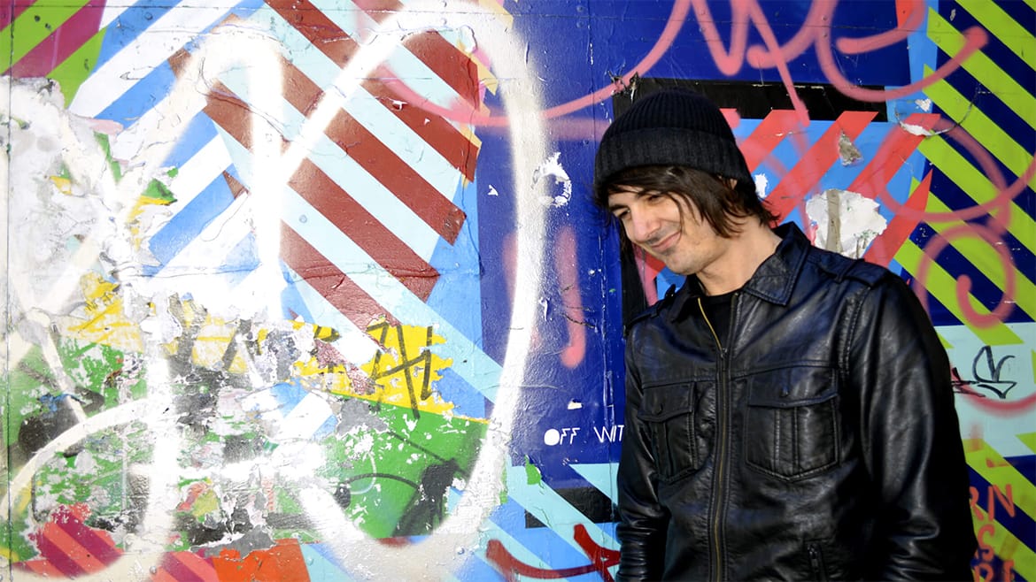 Daniel standing in front of a wall of street art, just off Brick Lane in London