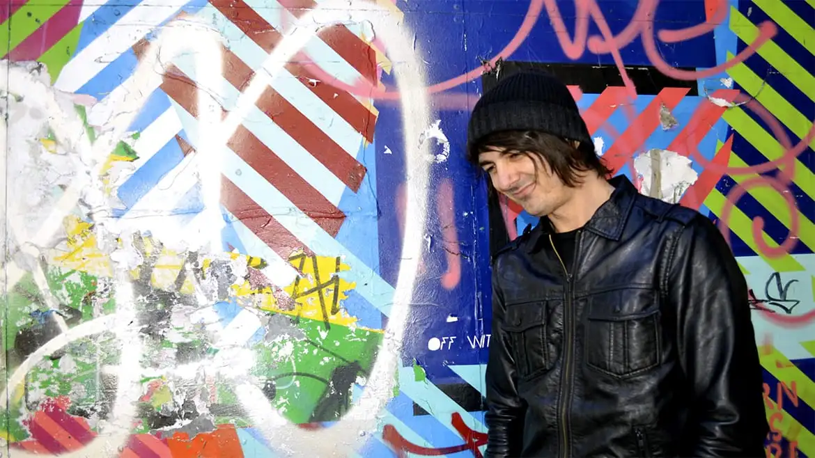 Daniel standing and laughing in front of a wall of street art, just off Brick Lane in London